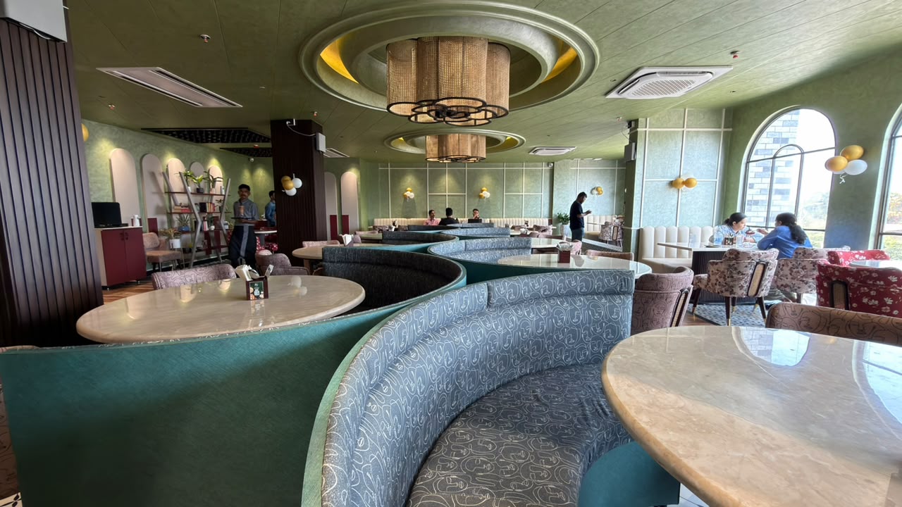 The dining room at Eight By Seven, with curved banquettes, marble tables, and cane chandeliers under a sage ceiling.