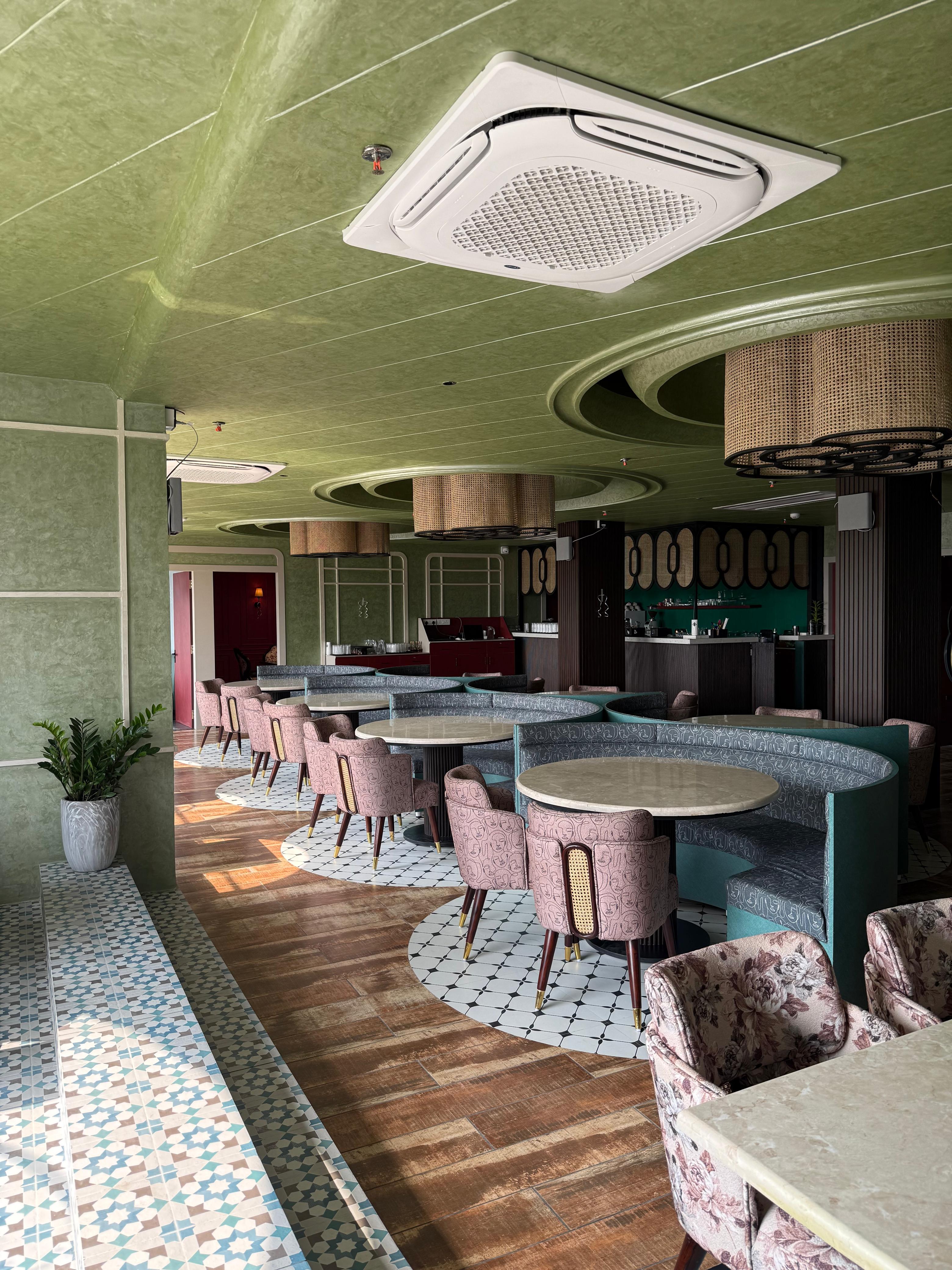Aisle of marble tables, pink patterned chairs, and a geometric tile floor.